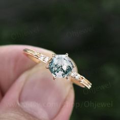 a close up of a person's hand holding an engagement ring with a green and white diamond