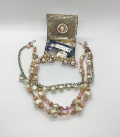 Vintage lot of 3, sold together only. 2 bead necklaces from the 50s and one pair of clip earrings. First necklace is a beautiful pink and dusty pink purple two-strand necklace with aurora borealis pink and textured creamy satin white faux pearls. Hook closure. 15-16 inches. Second necklace is a sparkly aurora borealis rhinestone and dimpled faux pearl necklace. About 15 inches. Clip earrings measure 1.5 inches long, made of elegant grayish purplish faux pearls and shimmering aurora borealis. Wea Vintage Beaded Jewelry For Party, Pink Multi-strand Jewelry For Party, Clip-on Costume Jewelry For Vintage Events, Handmade Vintage Pink Jewelry, Vintage Pink Beaded Necklace As A Gift, Party Costume Jewelry With Vintage Charm, Vintage Charm Costume Jewelry For Party, Vintage Pink Single Strand Jewelry, Vintage Pink Beaded Necklaces