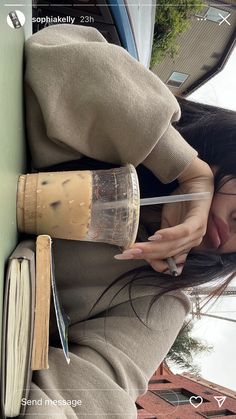 a woman leaning against a wall with an open book and coffee mug in her hand