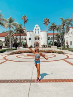 a woman standing in front of a white building with palm trees around her and arms outstretched