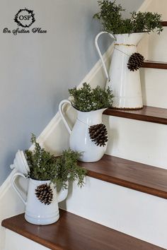 three white vases filled with pine cones on top of some wooden banisters