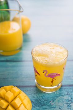 a glass filled with yellow liquid next to sliced mangoes and pineapples on a table