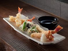 a white plate topped with sushi next to a black bowl on top of a wooden table