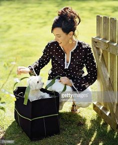 a woman sitting on the grass with her white dog in a black tote bag