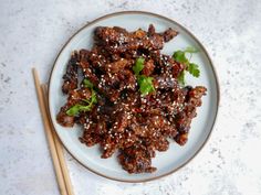 a white plate topped with meat covered in sesame seeds and garnished with cilantro