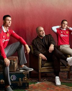 three men sitting on chairs in front of a red wall