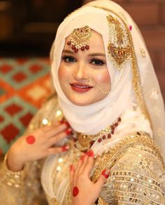 a woman wearing a white and gold outfit with red nail polish on her nails, posing for the camera