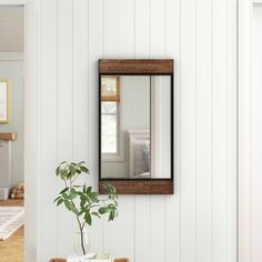 a mirror hanging on the wall above a table with a potted plant in it