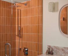 an orange tiled bathroom with a shower, mirror and soap dispenser on the wall