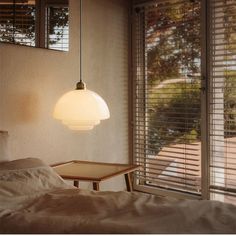 a lamp hanging over a bed next to a window with blinds on the outside wall