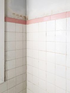 a bathroom with pink and white tiles on the walls, toilet paper is in the corner