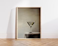 an image of a martini glass with olives in it sitting on a wooden floor