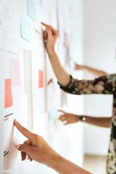 two women pointing at post - it notes on a wall