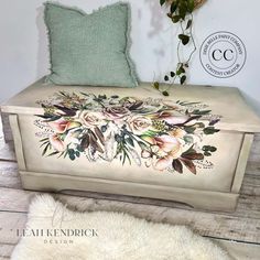 a white bench with flowers painted on it and a green pillow sitting next to it