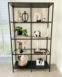 a black and white shelf with vases, candles and other items on it in front of a window