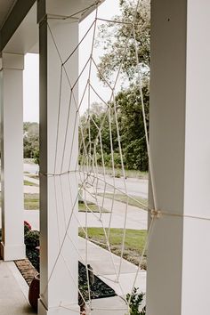 a spider web hanging from the side of a white building next to a sidewalk with potted plants