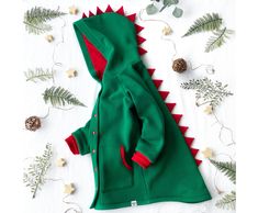 "A green baby dinosaur jacket is a great handmade gift for girls and boys.  The warm stegosaurus coat is suitable for walks on the street in spring or autumn. The kid's spring overcoat is made of fleece knitted fabric, which perfectly warms. The lining is made of jersey fabric.  In the front, there are two pockets for small treasures. The buttoned jacket is comfortable to wear for both parents and children. The soft toddler coat looks very fun and attractive. Contrasting spikes are fun and eye-catching.  The jacket is fully lined. The color of the lining matches the color of the spikes (red).  You can change the color of the lining by writing me a letter. I'll pick it up for you. Choose your dinosaur costume color.  It is hipster baby clothes. In the photo is my little Stephanie (purple di Playful Green Outerwear For Fall, Playful Green Long Sleeve Outerwear, Playful Green Winter Outerwear, Dinosaur Jacket, Costume Dinosaure, Rex Costume, T Rex Costume, Hipster Baby Clothes, Toddler Coat