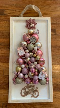 a christmas tree made out of ornaments in a white frame on a wooden floor with the words merry christmas written below it