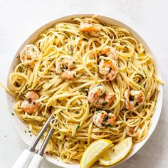 a white bowl filled with shrimp pasta and garnished with lemon wedges next to a pair of tongs