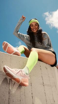 a woman sitting on top of a cement wall with her legs crossed and wearing tennis shoes