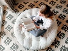 a woman reading a book while sitting on a bean bag chair