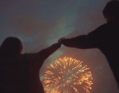 two people are holding hands with fireworks in the sky behind them and one person has their arms around the other