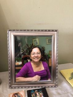 a woman sitting in front of a picture frame on a table with other items around her