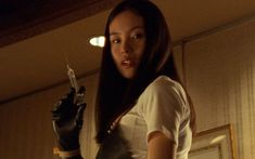 a woman in white shirt and black gloves holding a small syringe