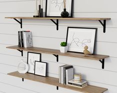 two wooden shelves with pictures and books on them next to a white wall in a living room