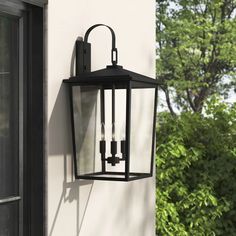 an outdoor light hanging on the side of a house with trees in the back ground