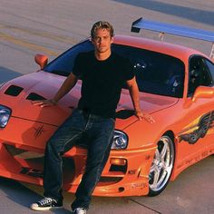 a man sitting on the hood of an orange sports car