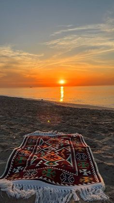 a blanket on the beach at sunset with the sun setting in the distance behind it