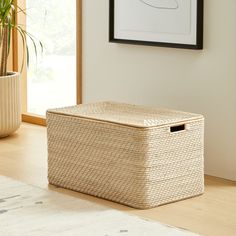 a wicker storage box sits on the floor next to a potted plant in front of a window