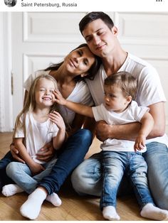 a man, woman and two children sitting on the floor with their arms around each other