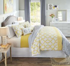 a white bed with yellow and gray comforter in a bright bedroom, next to a window