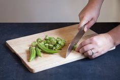 a person cutting green beans on a wooden cutting board with a chef's knife