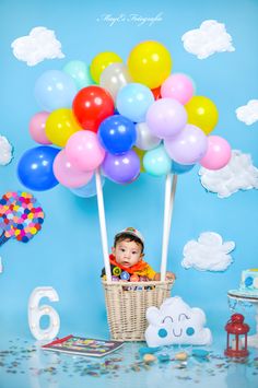 a baby is sitting in a basket with balloons on the top of it, surrounded by other toys