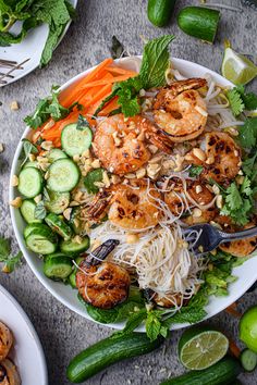 a bowl filled with shrimp and noodles next to cucumbers, carrots, and other vegetables