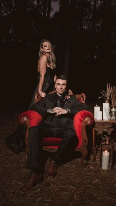 a man and woman are sitting on red chairs in the middle of a dark forest