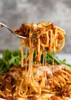 a fork full of spaghetti being lifted from a white plate with spinach and cheese