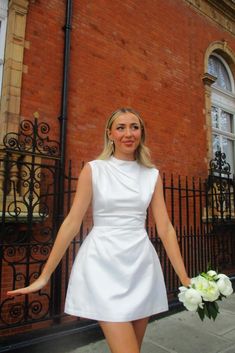 a woman standing in front of a brick building with her hands out and holding flowers