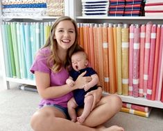 a woman sitting on the floor holding a baby in front of a book shelf filled with books