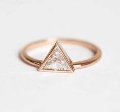 a rose gold ring with a triangle shaped diamond on the front and side, sitting on a white surface