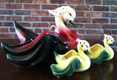 three ceramic birds sitting on top of a wooden table next to a brick wall,