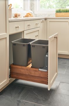 two trash cans sitting in the middle of a kitchen cabinet with an open pull out drawer