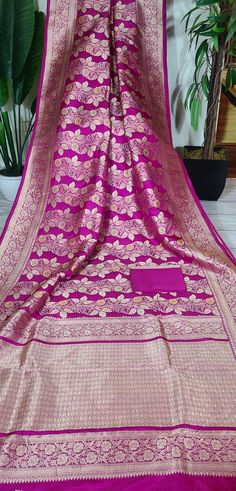 Magnificent saree from the Banarasi repertoire that showcases it's finery! A new design with rose creepers colored in meenakari silk form a standout design! Set in a lovely pink shade, the motifs beautifully stand out against the dark base! The base fabric is pure Katan silk that is known for its luster and softness! SILK MARK CERTIFIED The saree is ready to wear with falls and pico done. Hand-knotted tassels lend charm. An unstitched blouse fabric is included. *Note: There may be minor variatio Pink Chanderi Unstitched Suit For Transitional Season, Transitional Pink Dola Silk Salwar Kameez, Pink Dola Silk Dupatta In Traditional Drape, Pink Dola Silk Dupatta Traditional Drape, Pink Chanderi Unstitched Suit With Zari Work, Pink Chanderi Unstitched Suit For Navratri, Pink Dola Silk Traditional Dupatta, Pink Semi-stitched Dola Silk Unstitched Suit, Traditional Pink Dola Silk Dupatta