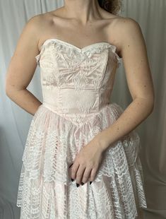 Details: maxi length; crinoline lining with blush pink and white lace, layered overlay; full, tiered skirt; dropped v-waist; strapless, sweetheart neckline; boning in bodice; zip-up closure in the back.  Damage: stain to front top layer of lace; lace appears slightly grayed in skirt overall; discoloration (dirt) to hemline).  Bust: 29 in // Waist: 25 in // Overall Length: 50 in Please note all inventory is pre-loved and sold as is. I will always do my absolute best to detail any and all damage i Pink Lace Corset Dress With Fitted Bodice, Pink Lace Corset Dress With Corset Back, Pink Lace Corset Dress For Prom, Pink Strapless Dress With Lined Bodice For Wedding, Pink Strapless Wedding Dress With Lined Bodice, Strapless Ruffled Dress For Debutante Ball, Pink Strapless Corset Dress For Debutante Ball, Pink Strapless Dress With Boned Bodice For Wedding, Feminine Strapless Corset Wedding Dress