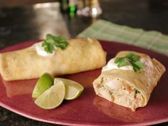 two burritos on a red plate with lime wedges and a green garnish