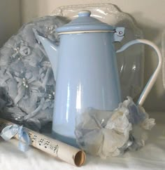 a blue tea pot sitting on top of a bed next to a pillow and some other items