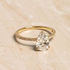 a yellow gold ring with a pear shaped diamond in the center and pave diamonds around it